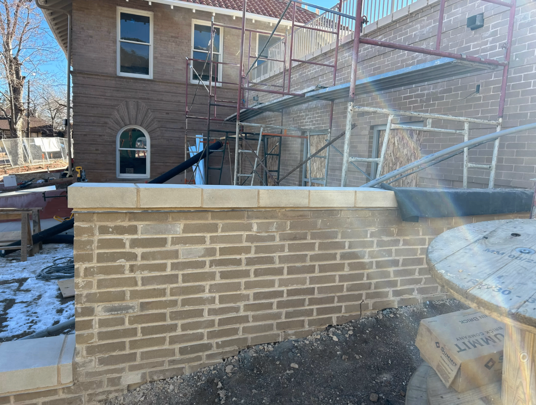 Tan brick wall with limestone cap in front of a historic brick building in Colorado